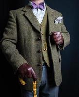 portret van Mens in tweed pak en leer handschoenen Holding paraplu Aan zwart achtergrond. klassiek en excentriek Engels heer. foto