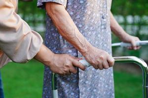 verzorger helpt aziatische oudere vrouw handicap patiënt lopen met rollator in park, medisch concept. foto