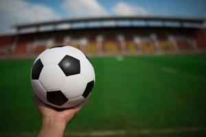 hand met een voetbal op gras met stadion achtergrond foto
