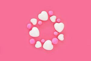 Valentijnsdag dag decoraties Aan roze achtergrond. wit schitteren harten en roze pluizig pompons geregeld in een cirkel, gecentreerd Aan helder roze papier. groet kaart met kopiëren ruimte. top visie, vlak leggen. foto
