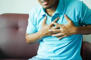 jonge man die pijn in het hart lijdt en de borst met de hand vasthoudt foto
