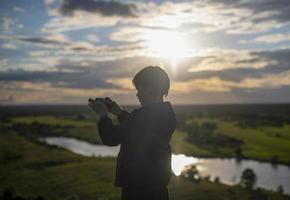 een jongen duurt afbeeldingen Aan zijn telefoon van een verbazingwekkend berg landschap met een meer gedurende zonsondergang. de jongen is aan het kijken natuur. vrijheid van levensstijl. foto