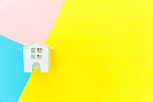 ontwerp eenvoudig met miniatuur wit speelgoedhuis geïsoleerd op blauw geel roze pastel kleurrijke trendy geometrische achtergrond hypotheek eigendom verzekering droom huis concept. plat lag bovenaanzicht kopieerruimte. foto
