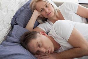 midden- oud vrouw aan het bedekken oren terwijl Mens snurken in bed foto