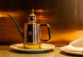 oud en antiek wijnoogst koper water werper of koffie pot met handgemaakt messing omgaan met Aan oud hout borden portie tafel in een oude historisch huis foto