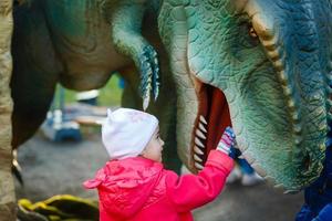 weinig meisje op zoek uit van de mond van een dinosaurus replica in een amusement park foto