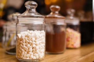 hoop van marshmallows in transparant glas pot Aan licht roze kleding achtergrond foto