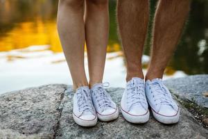 liefde verhaal vertelde door laarzen. menselijk voeten dichtbij omhoog. Mens en vrouw in sportschoenen. meisje in wit schoenen. vent in zwart sportschoenen en denim. hipster paar in zomer. poten dichtbij omhoog. foto