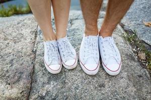 liefde verhaal vertelde door laarzen. menselijk voeten dichtbij omhoog. Mens en vrouw in sportschoenen. meisje in wit schoenen. vent in zwart sportschoenen en denim. hipster paar in zomer. poten dichtbij omhoog. foto