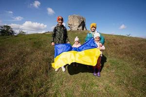 Welkom naar Oekraïne. vier kinderen houden oekraïens vlag in de buurt groot steen in heuvel pidkamin. foto