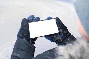 telefoon in jongen handen in horizontaal positie. jongen in een winter jasje, handschoenen en een kap. geïsoleerd Scherm voor model. winter tijd foto