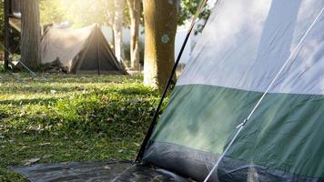 een hoek van een groen tent verspreiding uit Aan een zwart canvas onder de schaduw van een groot boom. achtergrond waren gazons en andere tenten in de afstand onder de ochtend- licht. foto