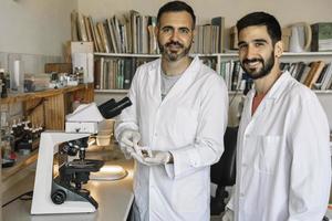 twee mannetje wetenschappers op zoek Bij camera en glimlachen in laboratorium jas. foto