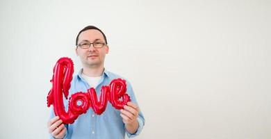 foto van knap Mens in bril in liefde Aan wit achtergrond met liefde ballon. valentijnsdag dag banier met plaats voor tekst