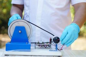 dichtbij omhoog handen slijtage blauw handschoenen demonstreren wetenschap experiment over elektriciteit stroomkring van dynamo uitrusting voor onderwijs. concept, wetenschap onderwerp, project werk. experiment, onderwijs. buitenshuis klas. foto