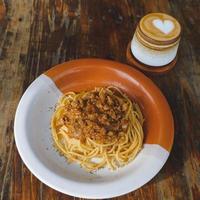 gezond bord van Italiaans spaghetti bekroond met een smakelijk tomaat en grond rundvlees bolognese saus en vers basilicum Aan een rustiek bruin houten tafel. geserveerd met cappuccino foto