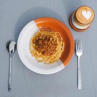 gezond bord van Italiaans spaghetti bekroond met een smakelijk tomaat en grond rundvlees bolognese saus en vers basilicum Aan een grijs tafel. geserveerd met cappuccino foto
