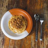 gezond bord van Italiaans spaghetti bekroond met een smakelijk tomaat en grond rundvlees bolognese saus en vers basilicum Aan een rustiek bruin houten tafel foto