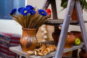 vaas met oren van tarwe Aan kokosnoot en houten achtergrond oren in een klei vaas, blauw bloemen, bagels foto