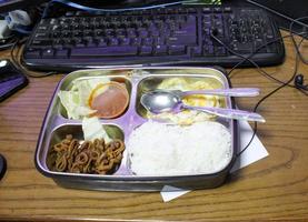 aan het eten Bij werk plaats met lunch doos in voorkant van computer foto