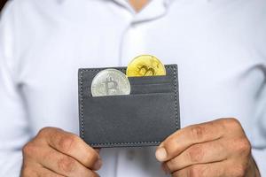 een Mens houdt metaal bitcoins in zijn handen in een grijs leer portemonnee. bitcoin - een modern virtueel het formulier van geld foto