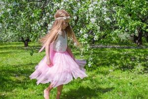 weinig schattig meisje met vlinder Vleugels hebben pret in bloeiende appel boomgaard foto