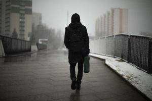 vent met diplomaat wandelingen naar beneden straat. Mens in zwart kleren in stad. bewolkt weer in middag. foto