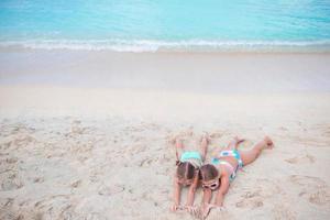 schattig weinig meisjes Aan zanderig strand. gelukkig kinderen aan het liegen Aan warm wit zanderig strand foto
