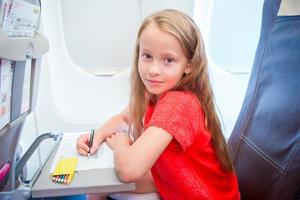 aanbiddelijk weinig meisje op reis door een vliegtuig. kind tekening afbeelding met kleurrijk potloden zittend in de buurt vliegtuig venster foto