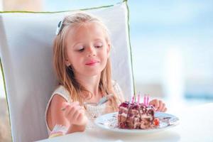 weinig meisje vieren gelukkig verjaardag met smakelijk taart in buitenshuis cafe foto