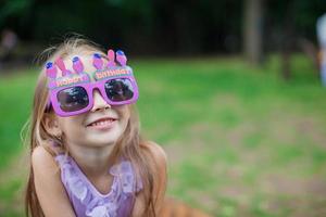 schattig weinig meisje in Purper gelukkig verjaardag bril glimlachen foto