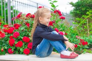 schattig weinig meisje in de buurt de bloemen in werf van haar huis foto