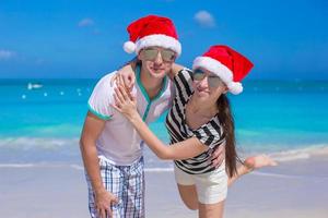 portret van een jong koppel in santa hoeden genieten van strandvakantie foto