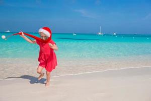 weinig aanbiddelijk meisje in rood de kerstman hoed hebben pret Aan de strand foto