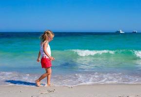 aanbiddelijk weinig meisje spelen in Ondiep water Bij wit strand foto