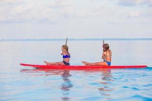 weinig schattig meisjes zwemmen Aan surfboard gedurende zomer vakantie foto