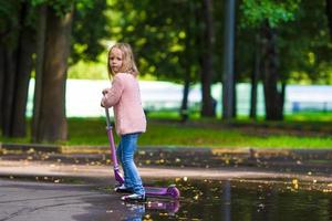 aanbiddelijk weinig meisje hebben pret Aan de scooter buitenshuis foto