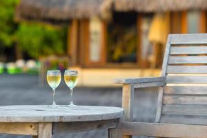 twee bril van smakelijk wit wijn Bij zonsondergang Aan houten tafel foto