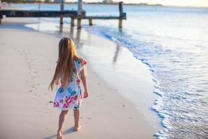aanbiddelijk weinig meisje wandelen Bij wit tropisch strand Aan zonsondergang foto