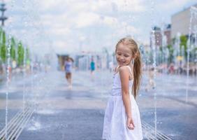 weinig meisje hebben pret in Open straat fontein Bij heet zomer dag foto