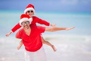 vader en dochter in de kerstman hoed hebben pret Bij tropisch strand foto