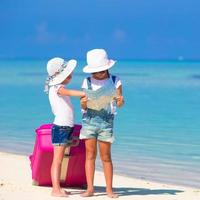 weinig meisjes met groot koffer en kaart Bij tropisch strand foto