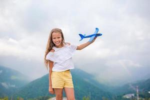 gelukkig weinig meisje met speelgoed- vliegtuig in handen in bergen foto