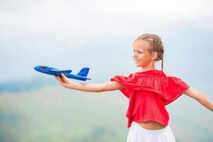 gelukkig weinig meisje met speelgoed- vliegtuig in handen in bergen foto