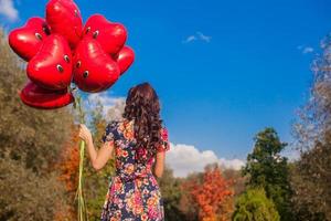 terug visie van aantrekkelijk jong meisje met rood glimlachen ballonnen in hand- buitenshuis foto