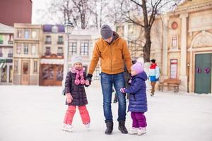 weinig meisjes met jong vader genieten van het schaatsen foto
