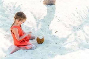 weinig aanbiddelijk meisje met groot kokosnoot Aan de strand foto