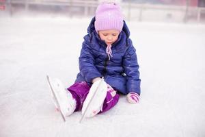 weinig verdrietig meisje zittend Aan een het schaatsen baan na de vallen foto