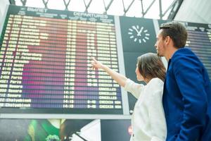 jong paar in Internationale luchthaven op zoek Bij de vlucht informatie bord foto