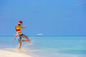 weinig meisje en jong moeder in de kerstman hoed gedurende strand vakantie foto